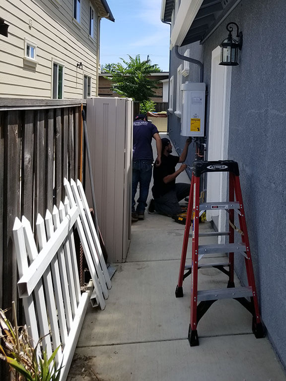 Plumbers install a Noritz tankless water heater on a side yard